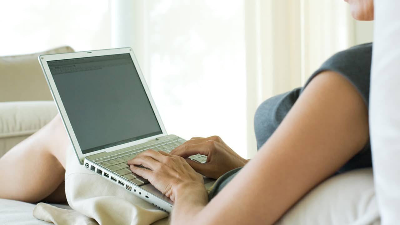 Nainen istuu sohvalla ja käyttää kannettavaa tietokonetta.