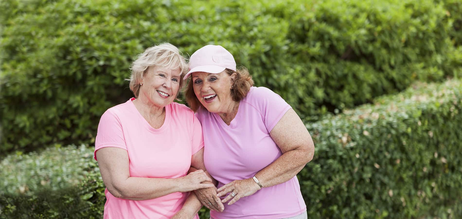 Kaksi iäkästä naista nauraa pinkeissä paidoissaan.