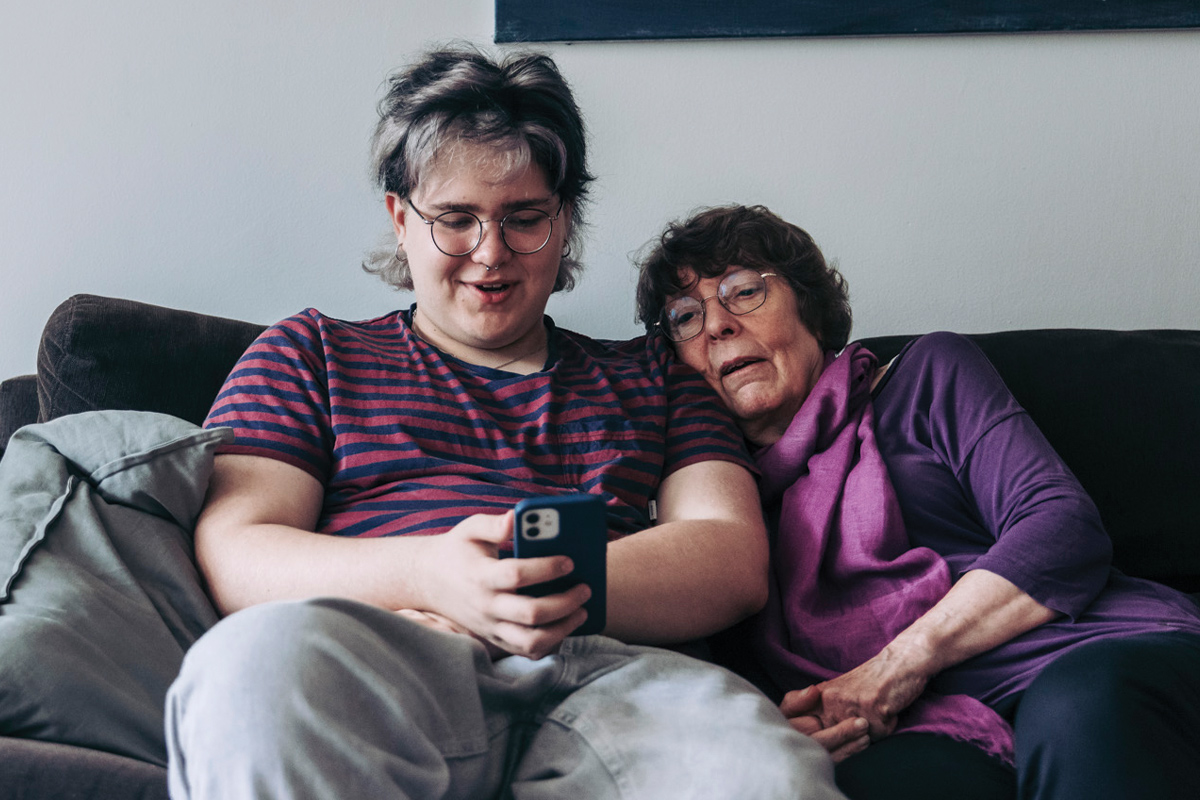 Teinipoika ja vanhempi nainen sohvalla katsoo yhdessä puhelimen näyttöä